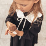 dziewczynka w czarnej sukience z kołnierzykiem je czekoladowego loda