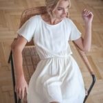 kobieta relaksuje się na wiklinowym krześle w śmietankowej sukience